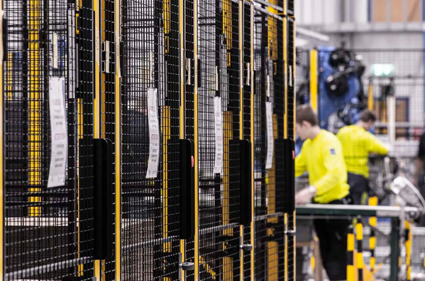 Arbetare i en fabrik, bredvid svart-gula säkerhetsbarriärer med metallnätpaneler