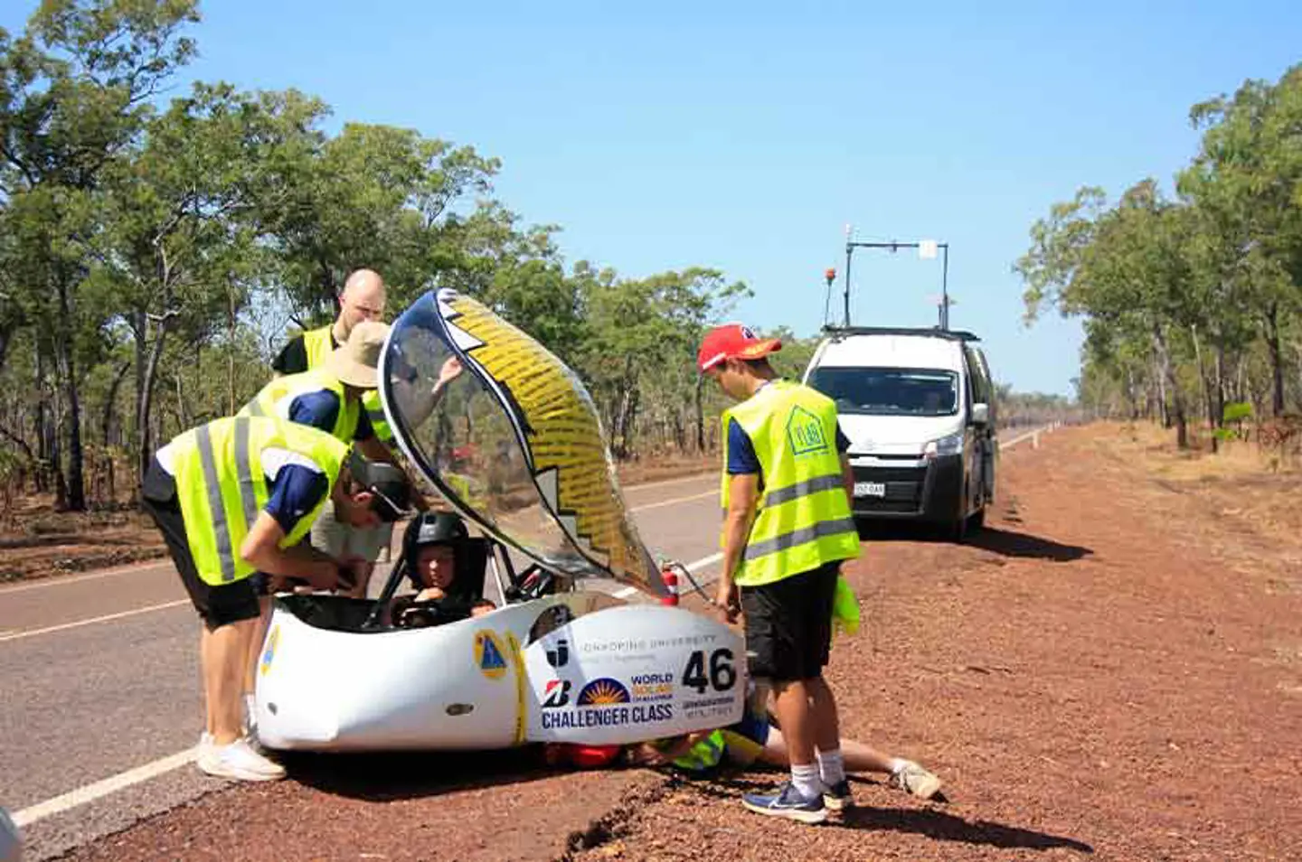 Tre medlemmar av JU Solar Team 2025 arbetar med solbilen Nova Lumia vid sidan av en väg i Australien.