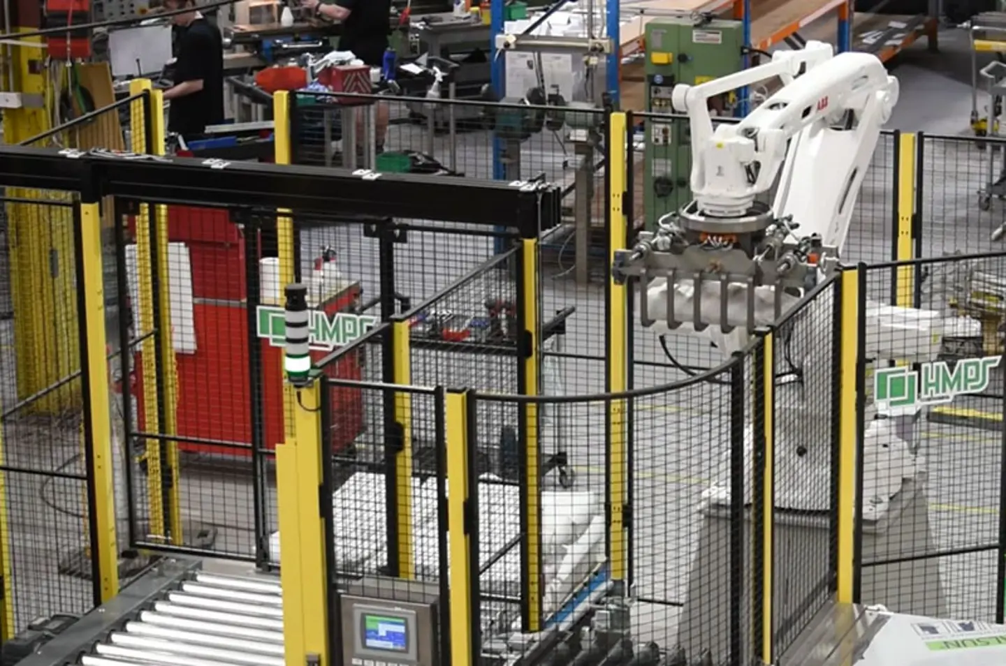 Automatiserad industrirobotarm som arbetar i en fabrik med transportbandssystem och säkerhetsstaket