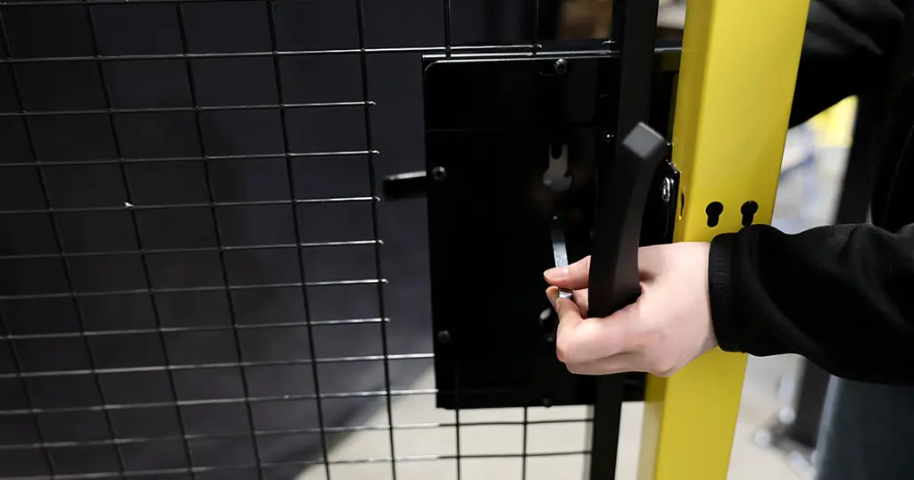 Hand som håller i ett cylinderhandtagslås monterat på en svart nätpanel